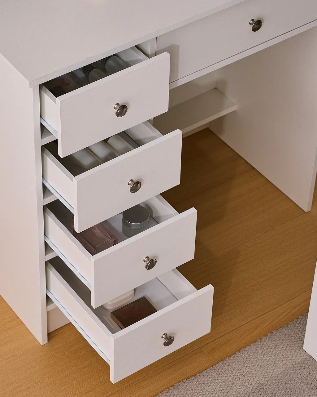 Dresser with four open drawers, showcasing a white finish and sleek silver knobs, placed on light wooden flooring.