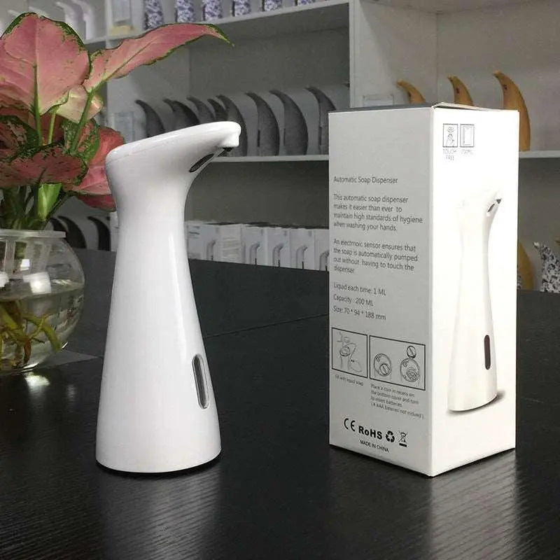 Sleek white automatic induction soap dispenser with an infrared sensor, placed beside a potted plant and product packaging.