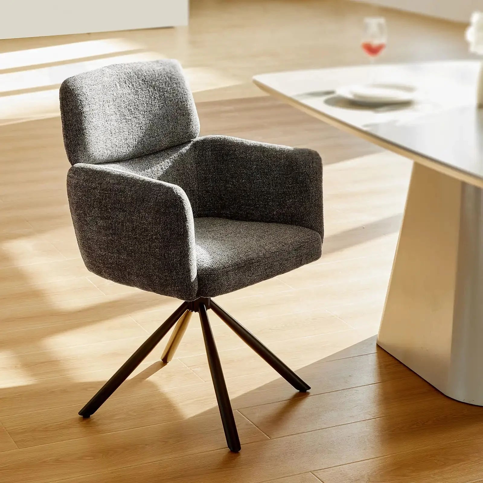 Smoky grey chenille swivel chair with a padded back and arms, supported by a black metal base, positioned near a dining table.