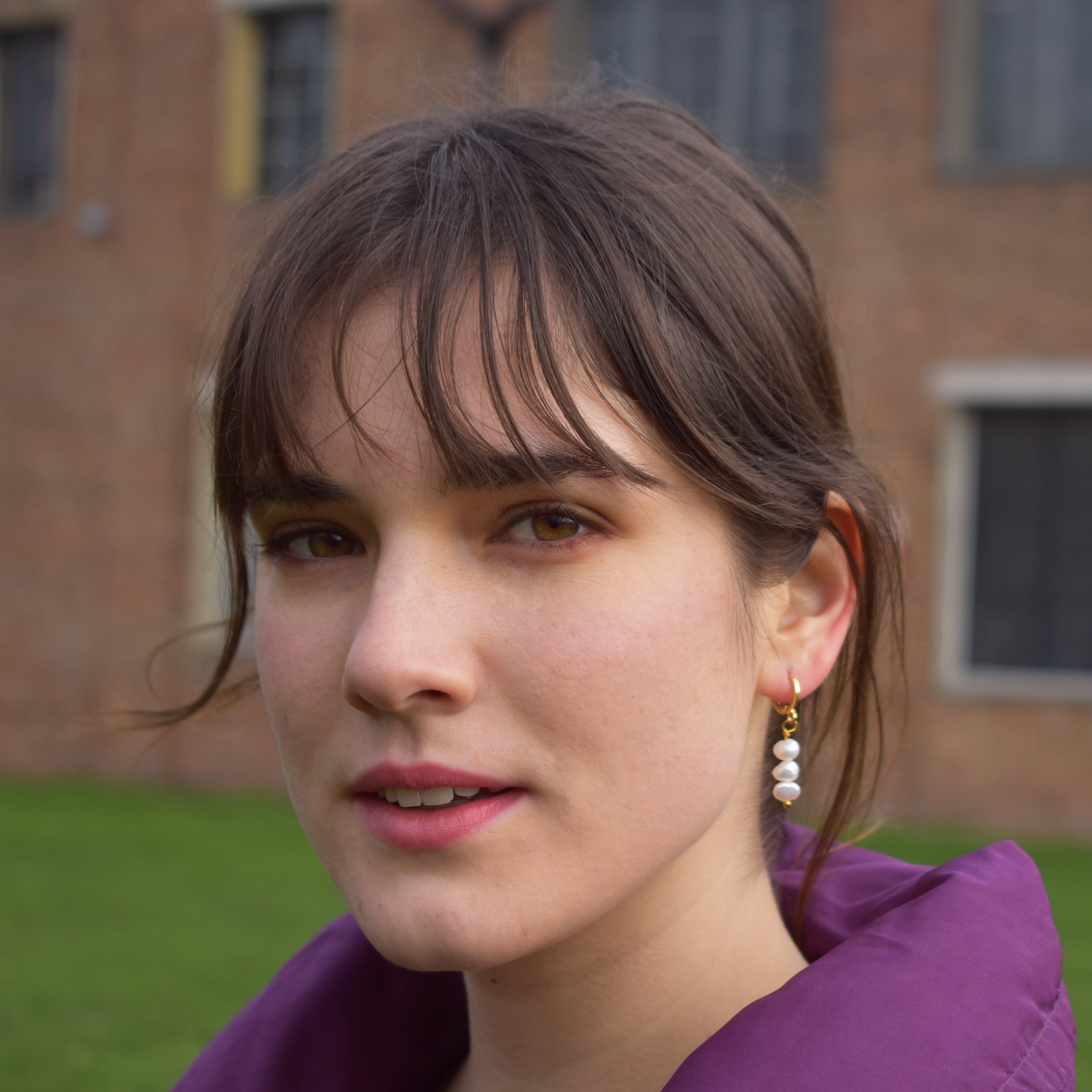 Triple irregular white freshwater pearl earrings with gold plated brass huggies, worn on a model's ear.