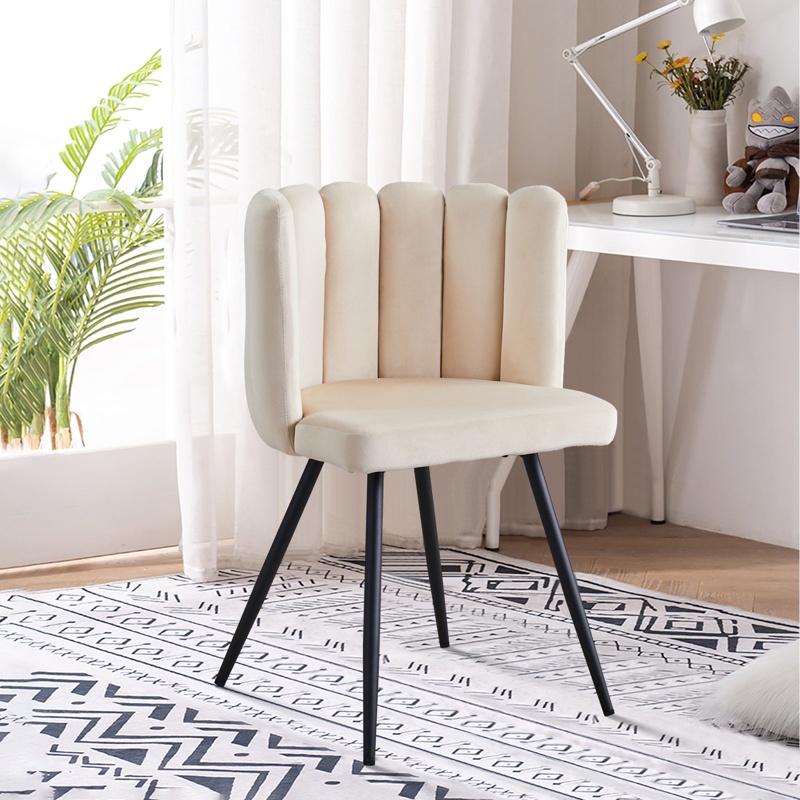 Cream-colored velvet accent chair with a petal curved backrest and black metal legs, set against a bright room.