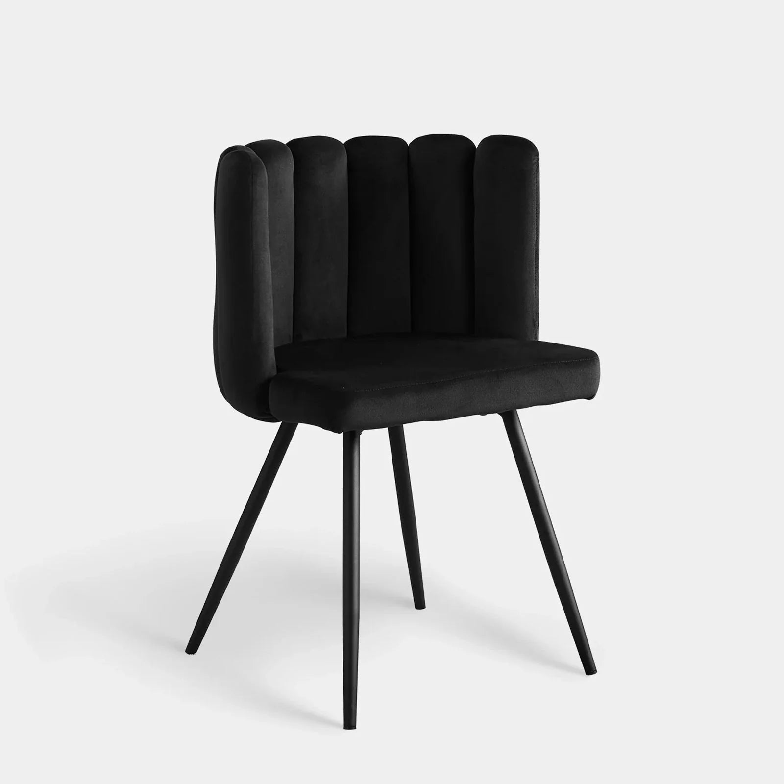 Black velvet dining chair with a petal curved backrest, vertical tufting, and tapered black metal legs.