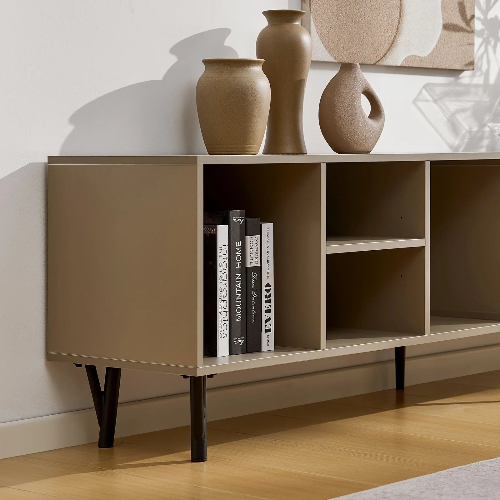 Extendable Milano TV stand in sand beige with six shelves, supported by black iron legs. Features books and vases on top.
