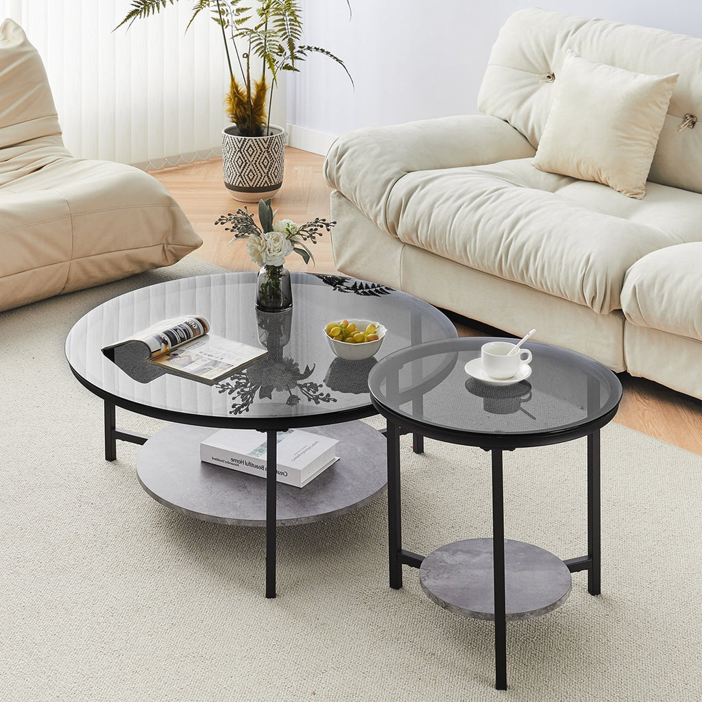 Black tempered glass coffee table set with round tops, metal legs, and a grey marble bottom shelf, styled in a living room.