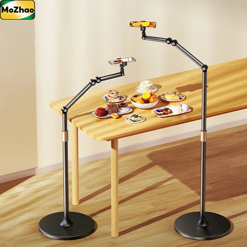Retractable aluminium floor stand with adjustable arms, shown holding tablets above a table with assorted desserts.
