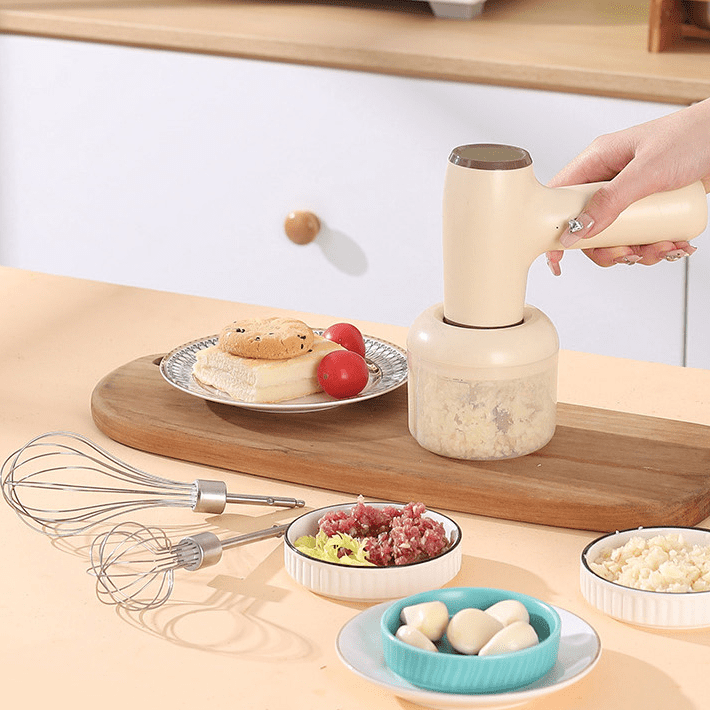 Khaki USB rechargeable garlic chopper held in hand, with finely chopped garlic in the container, surrounded by ingredients on a wooden board.