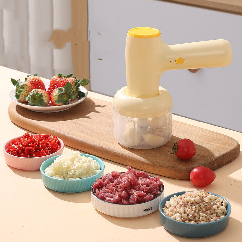 Khaki USB rechargeable garlic chopper on wooden cutting board, adjacent to chopped garlic, chili, meat, and strawberries.