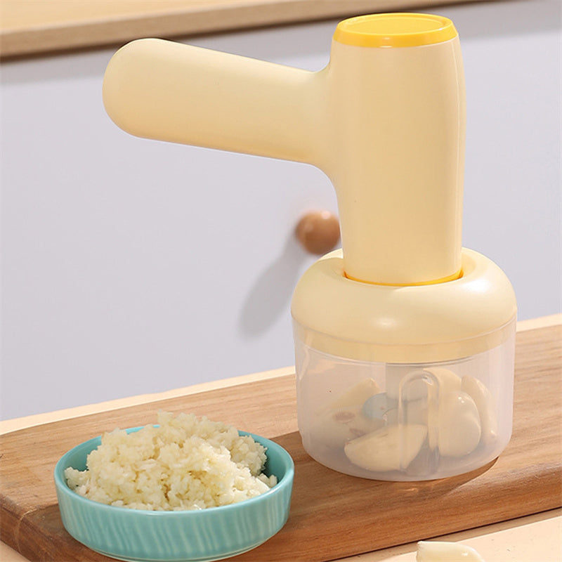 Khaki handheld USB rechargeable garlic chopper with a transparent cup and garlic cloves inside, next to a bowl of minced garlic.