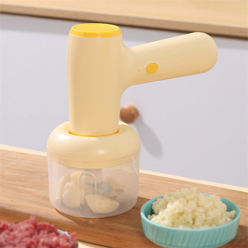 USB rechargeable garlic chopper in light yellow, with a clear cup holding chopped garlic, on a wooden surface.