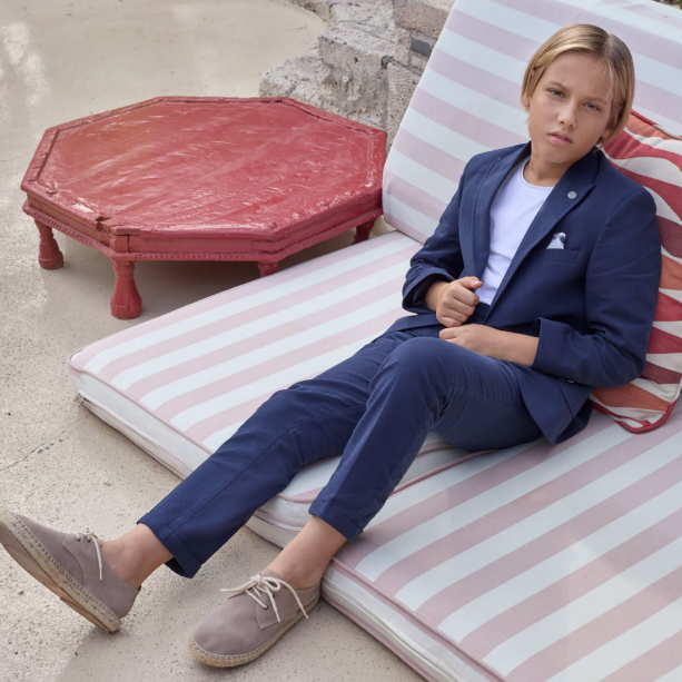 Navy blue tailored boys' suit with a structured blazer and matching trousers, worn with a white shirt and casual shoes.