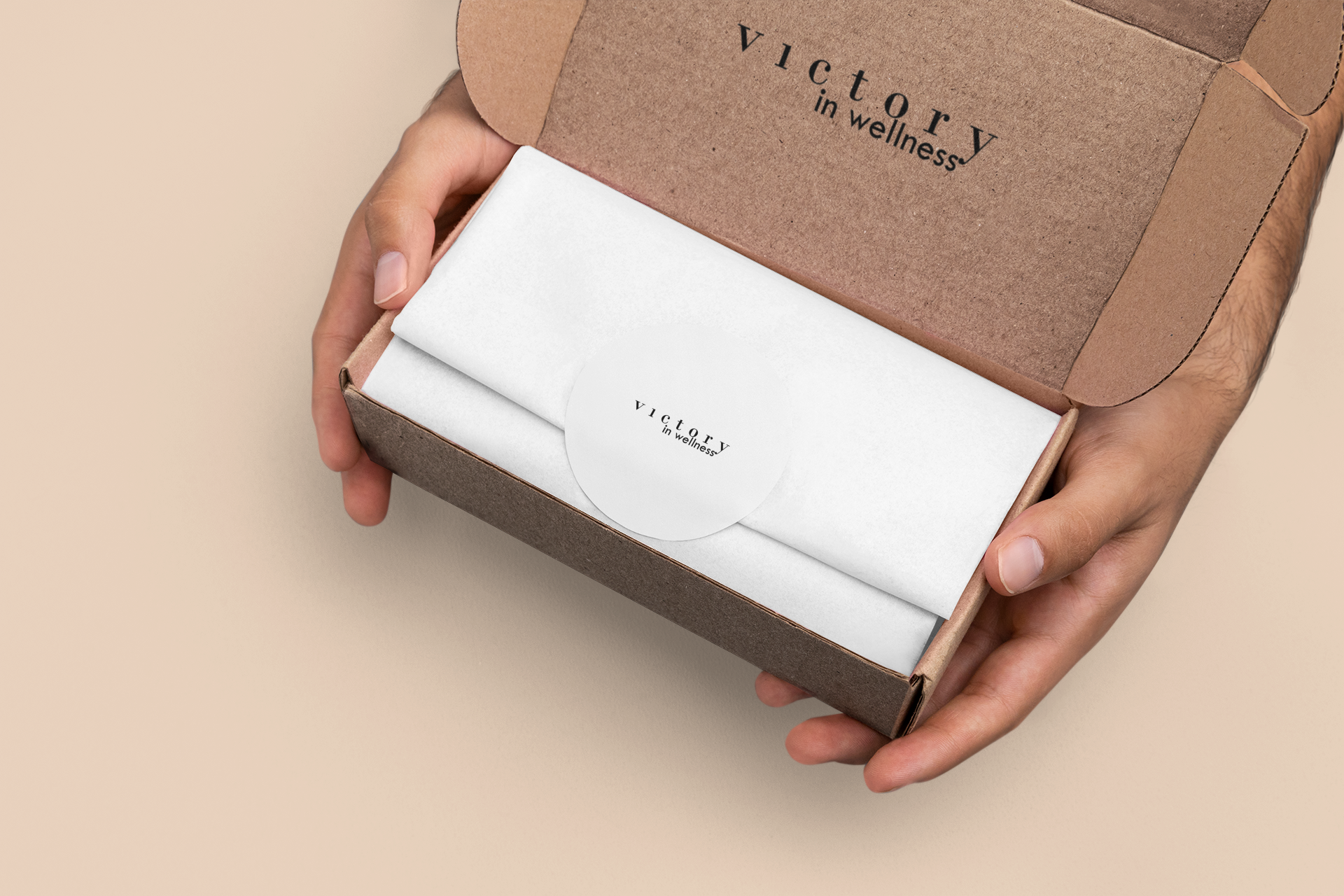 Hands hold a brown box open, revealing white tissue paper and a circular sticker with "victory in wellness" text inside.